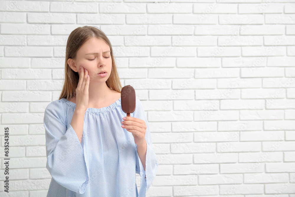 Young woman with sensitive teeth and ice-cream on white brick background Young woman with sensitive teeth and ice-cream on white brick background