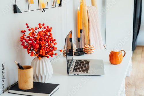 Obraz na plátne Home office desk with laptop, pumpkin shaped cup with hot drink and marshmallows, seasonal decor like candles, flowers, pumpkins
