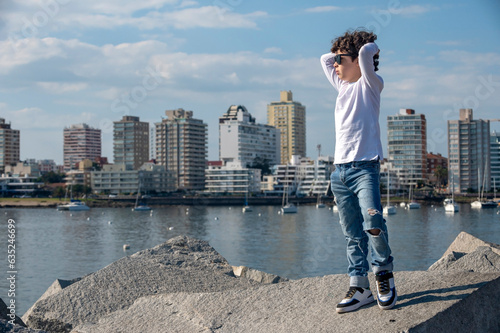 Boy in jeans and white pants with sunglasses posing for a photo in fashion editorial on the beach photo
