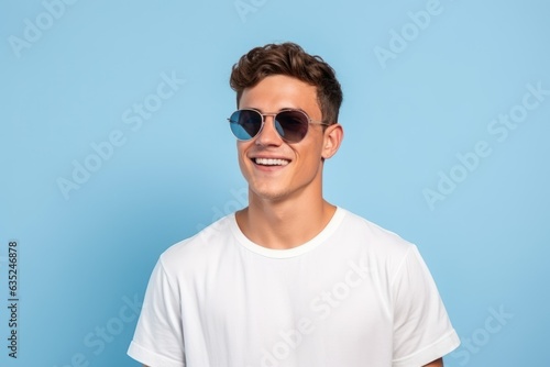 Young handsome and cool fictional person portrait. Guy smiling in casual white t-shirt. Isolated on a plain blue background. Generative AI. © Tuyres
