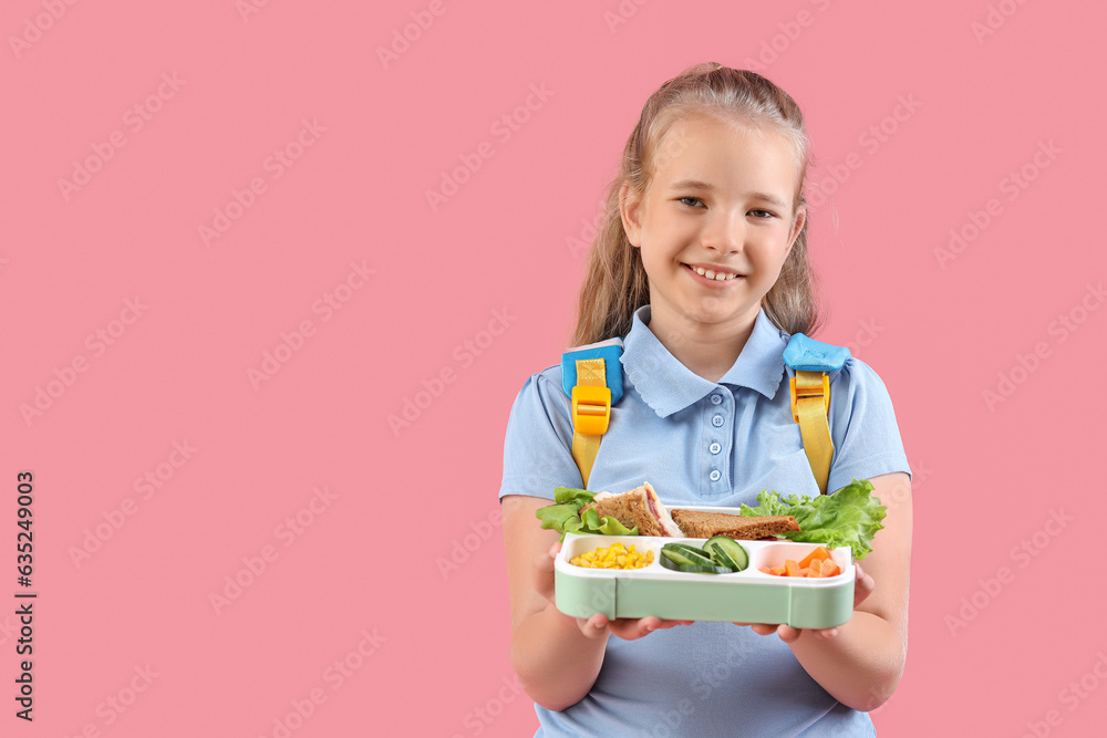 Happy little girl with backpack and lunchbox on pink background