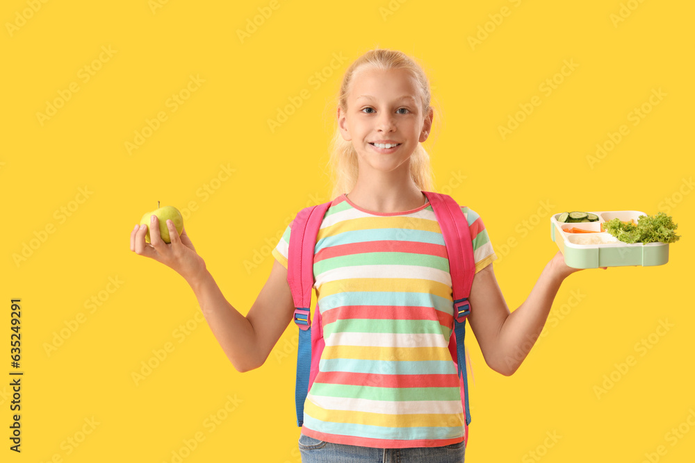 Happy girl with backpack, lunchbox and fresh apple on yellow background Happy girl with backpack, lunchbox and fresh apple on yellow background