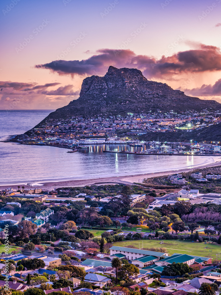 Aerial vertical shot of Hout Bay town, harbour, mountain and the beach during sunset, Western Cape, South Africa