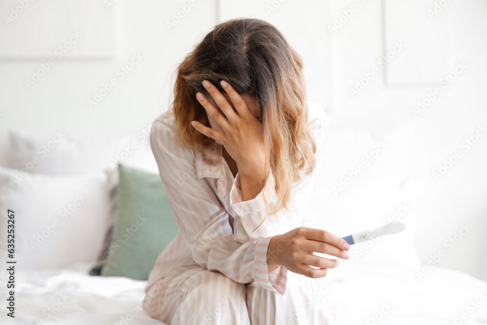 Upset young woman with pregnancy test in bedroom Upset young woman with pregnancy test in bedroom