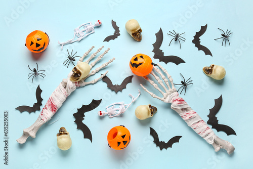 Composition with skeleton hands, skulls, pumpkins, paper bats and spiders for Halloween celebration on blue background