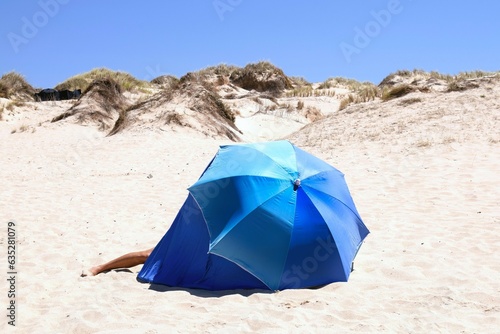 Blue parasol and tent close-up with man s leg sticking out . Sandy beach scene in Peniche  Portugal.
