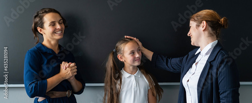 The teacher praises the schoolgirl in front of her mother standing at the blackboard.  photo