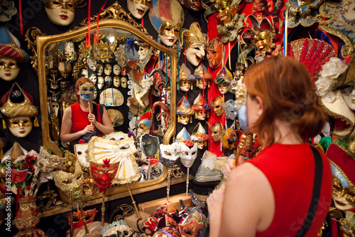 A tourist wears a souvenir painted mask in a shop for Venice Carnival (Carnevale di Venezia). photo