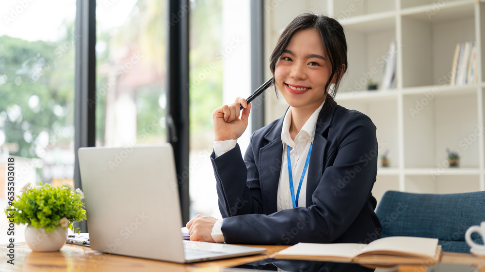 An attractive Asian businesswoman or female accountant in a formal business suit sits at her desk