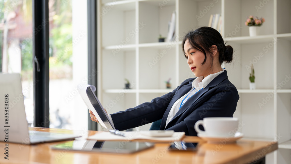 A focused and professional Asian businesswoman is examining a business report in her office. A focused and professional Asian businesswoman is examining a business report in her office.