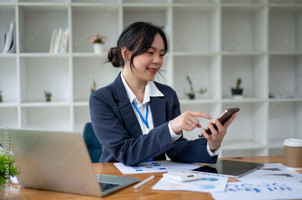 A happy Asian businesswoman using her smartphone at her desk in her private office. A happy Asian businesswoman using her smartphone at her desk in her private office.