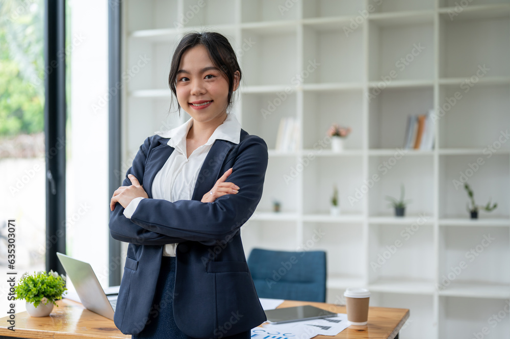 A confident Asian businesswoman smiling at the camera and standing with her arms crossed A confident Asian businesswoman smiling at the camera and standing with her arms crossed