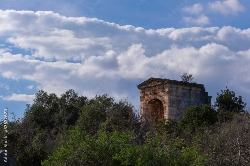 A Roman civilization artifact, located amidst the greenery in Anatolia, stands beautifully illuminated by the sun, casting its rays from the cloudy blue sky. A Roman civilization artifact, located amidst the greenery in Anatolia, stands beautifully illuminated by the sun, casting its rays from the cloudy blue sky.