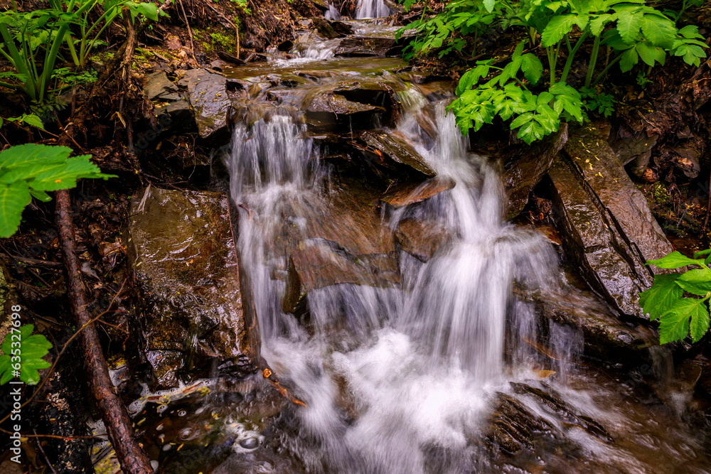 picturesque waterfall on a stream running from the mountains along a ravine on a spring day picturesque waterfall on a stream running from the mountains along a ravine on a spring day