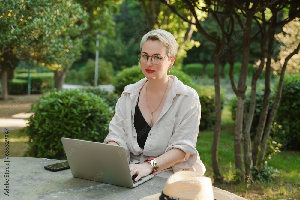 woman freelancer in glasses works at a computer at a white table in nature and spends her day productively woman freelancer in glasses works at a computer at a white table in nature and spends her day productively