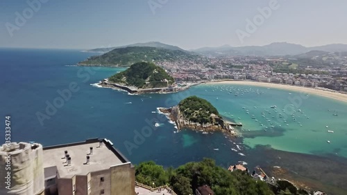 Aerial shot flying over the Monte Igeldo's Tower to Santa Clara Island situated in La Concha Bay.  In the background is the historic town of San Sebastian (Donostia), Spain on the Cantabrian Sea.