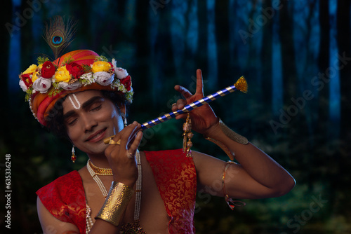 Close-up portrait of young man dressed up as Lord Krishna and playing flute on the occasion of Janmashtami photo