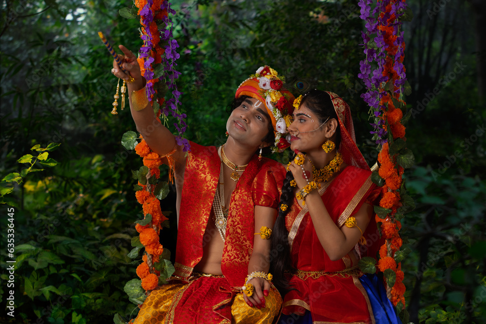 Young man and woman dressed up as Radha and Krishna and sitting together on a swing on the occasion of Janmashtami Young man and woman dressed up as Radha and Krishna and sitting together on a swing on the occasion of Janmashtami
