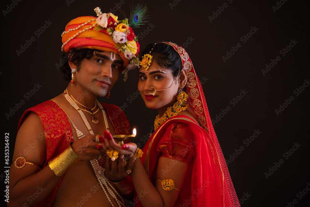 Young man and woman dressed up as Lord Radha and Krishna and holding diya together on the occasion of Janmashtami Young man and woman dressed up as Lord Radha and Krishna and holding diya together on the occasion of Janmashtami