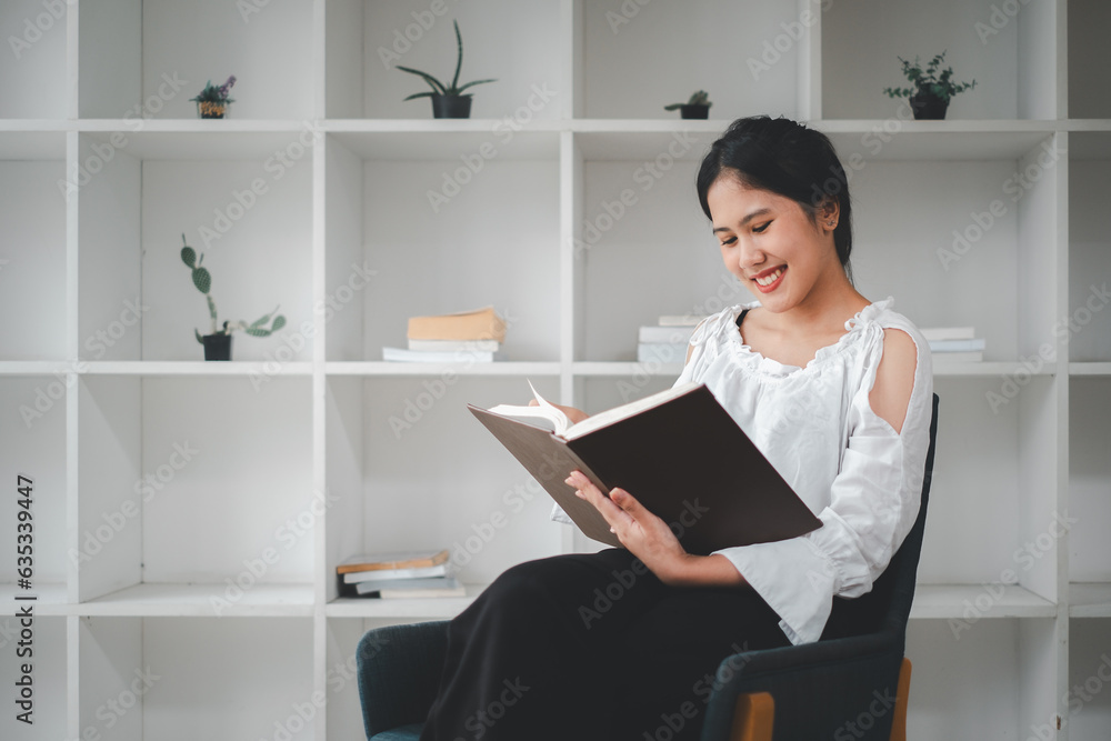 Side view of asian woman sitting armchair with open book and reading in living room. Side view of asian woman sitting armchair with open book and reading in living room.