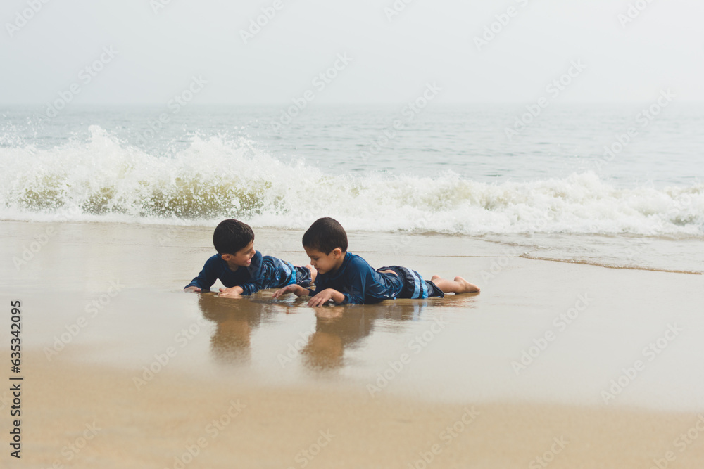 Young boys playing in sand and waves on beach.