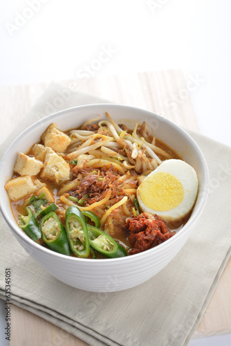 Malay mee rebus noodle with boiled egg, tofu, green chilli, sambal, vegetable, chilli sauce and hot thick spicy gravy soup in bowl on white background asian halal food cuisine menu for cafe design