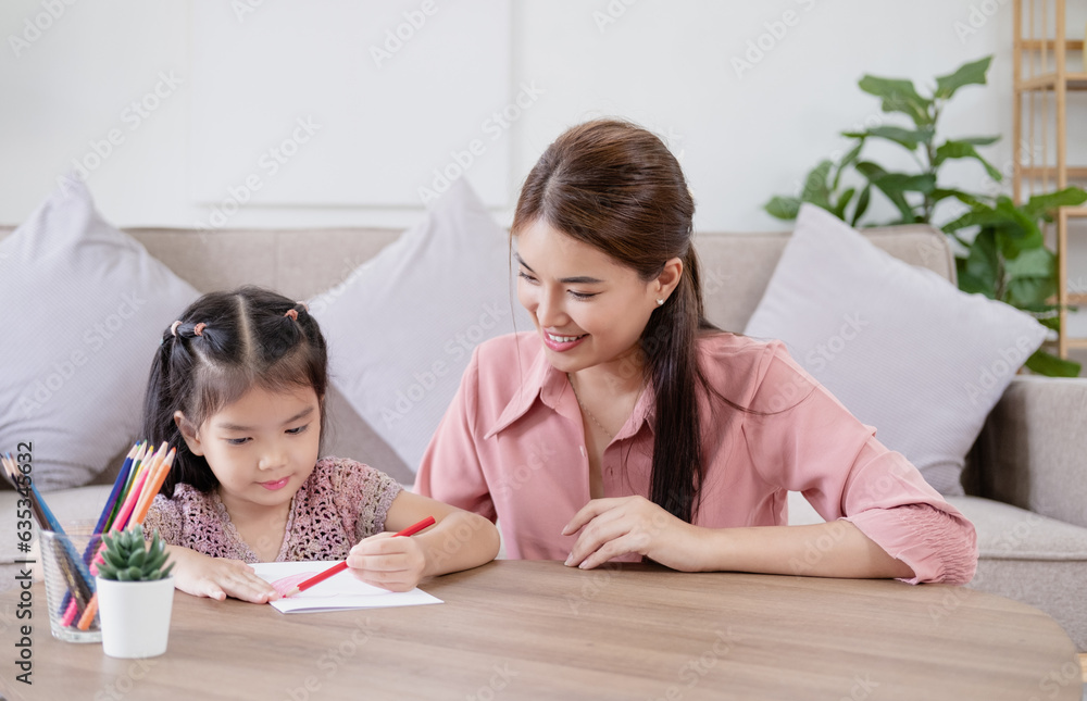 Happy asian young mother smile with daughter in living room at home. Asian young mother teaching small daughter to drawing reading and writing to develop her daughter skill. Home School Concept Happy asian young mother smile with daughter in living room at home. Asian young mother teaching small daughter to drawing reading and writing to develop her daughter skill. Home School Concept