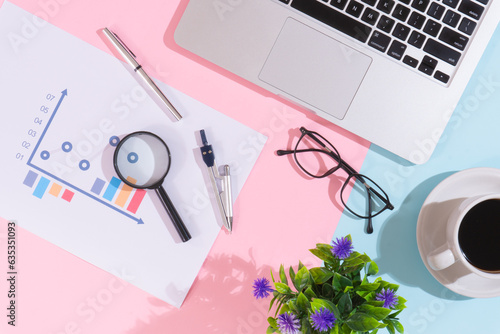 Flowering plant and coffee cup on office desk with laptop, pink and blue background
 photo