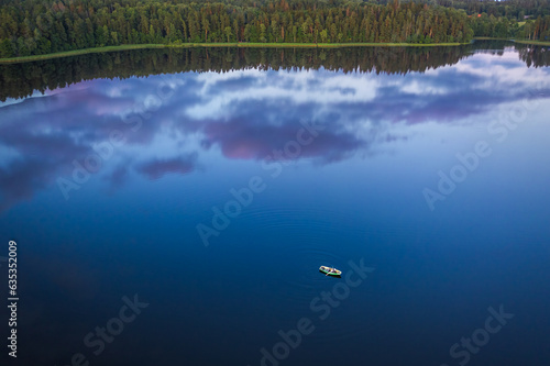 Row boat in the middle of dark lake. Cloud reflections in deep blue water. Abstract drone footage.