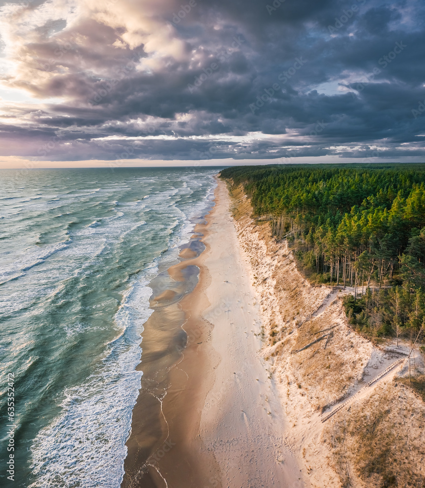 Baltic sea in colorful sunset colors with storm clouds. Turquoise water with waves, and sandy coastline.