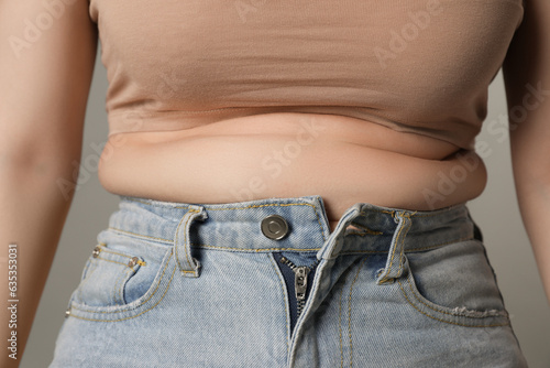 Overweight woman in tight jeans on grey background, closeup