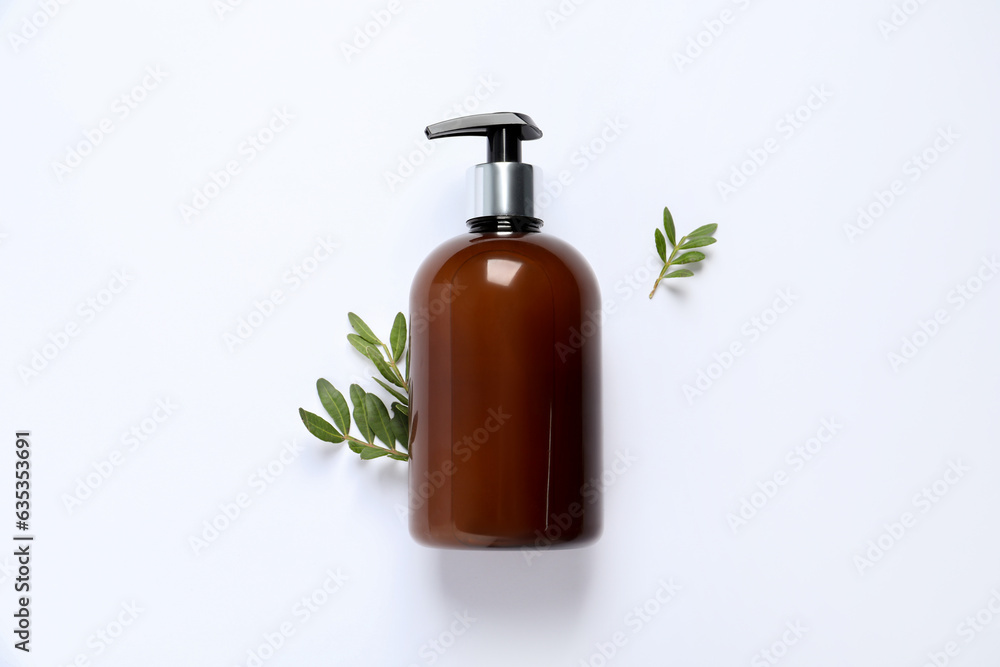 Bottle of cosmetic product and green leaves on white background, flat lay