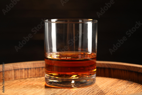 Glass of tasty whiskey on wooden barrel, closeup