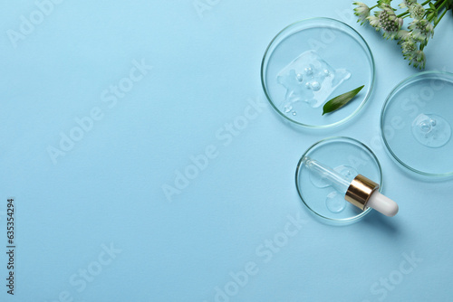 Petri dishes with samples of cosmetic oil, pipette and flowers on light blue background, flat lay. Space for text