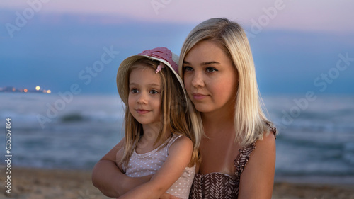 Mother and little daughter on beach of sea or ocean in evening at sunset. Summer vacation  travel  holiday. People outdoors