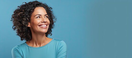 A Brazilian woman in her mid life presenting an idea with a smile while standing alone on a blue background