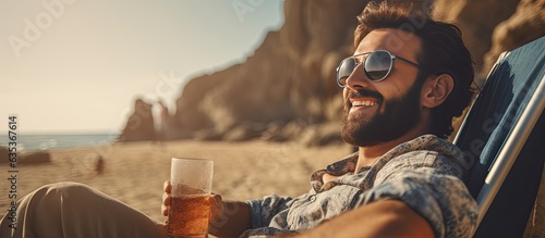 Young man sitting on beach rocks near ocean smiling and relaxing on camping chair enjoying his time in sunglasses