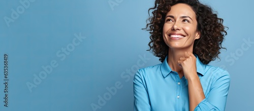 Obraz na płótnie A Brazilian woman in her mid life presenting an idea with a smile while standing alone on a blue background w salonie