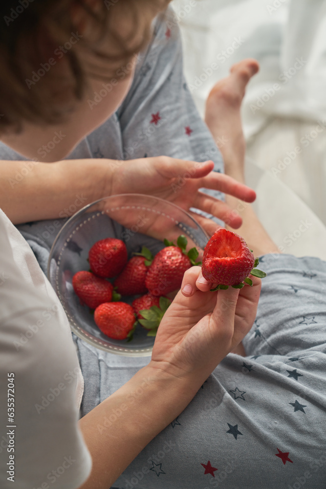 Crop kid eating strawberries from bowl at home Crop kid eating strawberries from bowl at home