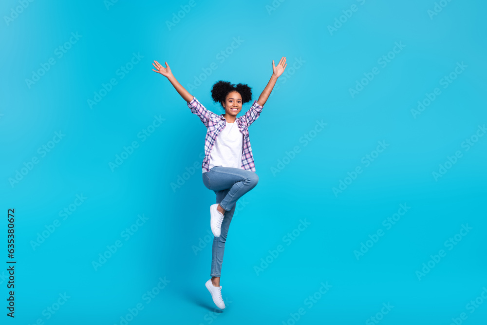 Full length photo of funky excited girl dressed checkered shirt jumping high rising arms isolated blue color background