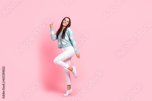 Full length photo of funky cheerful woman dressed blue cardigan showing v-sign empty space isolated pink color background