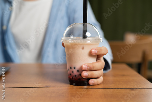 Man holding bubble milk tea in a plastic cup while sitting at a table in a restaurant