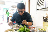 A man using chopsticks and spoon eating traditional Pho Bo vietnamese soup with beef and rice noodles on a metal table, real scene in local restaurant
