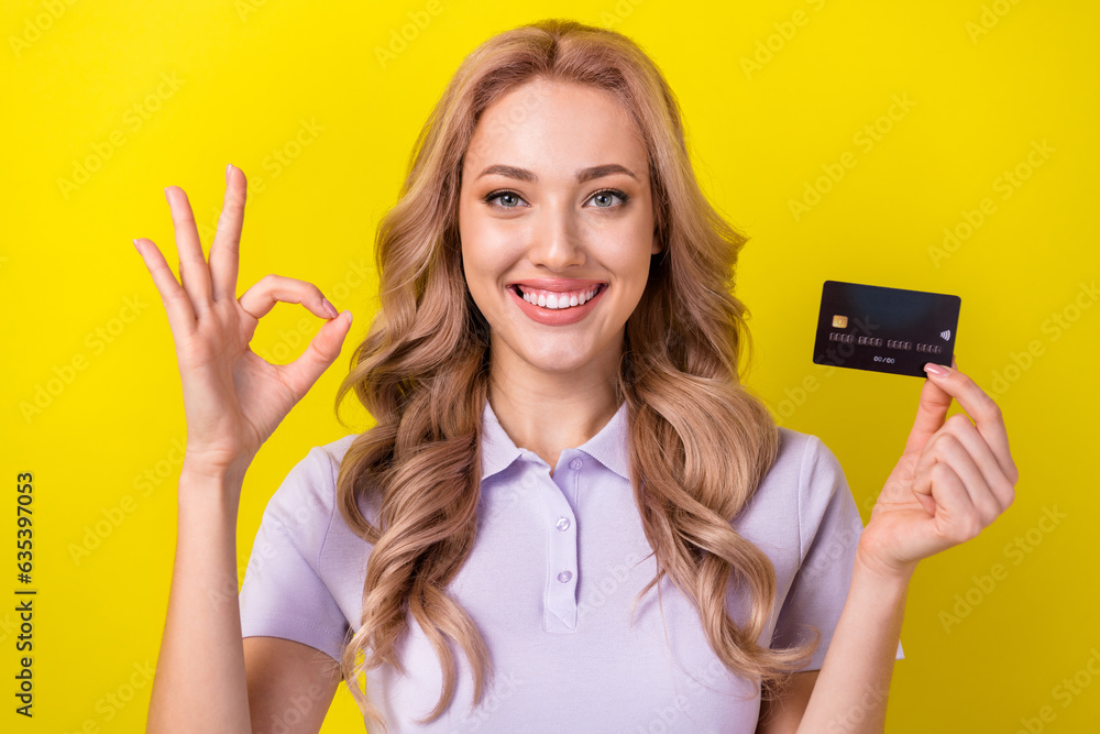 Portrait of charming cheerful lady toothy smile demonstrate okey symbol hold plastic debit card isolated on yellow color background Portrait of charming cheerful lady toothy smile demonstrate okey symbol hold plastic debit card isolated on yellow color background