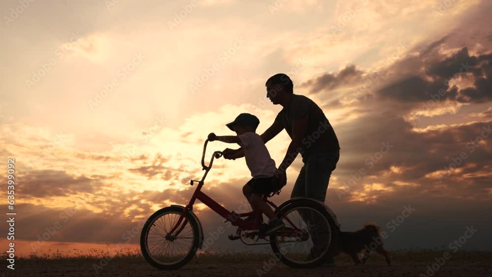 happy family in the park. father teaching son to ride a bike at sunset silhouette in the park. son child learning to ride a bike at sunset father helping son. child playing riding a lifestyle bike happy family in the park. father teaching son to ride a bike at sunset silhouette in the park. son child learning to ride a bike at sunset father helping son. child playing riding a lifestyle bike