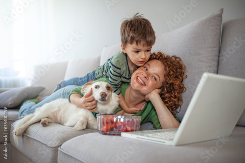 Mother and son with dog using laptop in living room and eating strawberries. Mother and son using laptop at home. Mother and son spending time together
