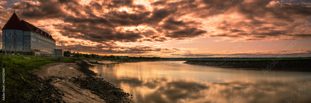 Petitcodiac River with dramatic sunrise cloudscape at Bore Park or Parc Bore Riverfront Walk, a popular place to watch the tidal bore in Moncton, New Brunswick, Canada