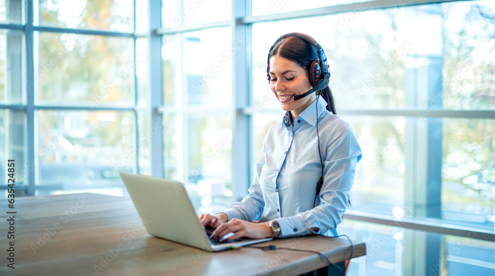 Beautiful female consultant of call center in headphones working on laptop at office. Beautiful female consultant of call center in headphones working on laptop at office.