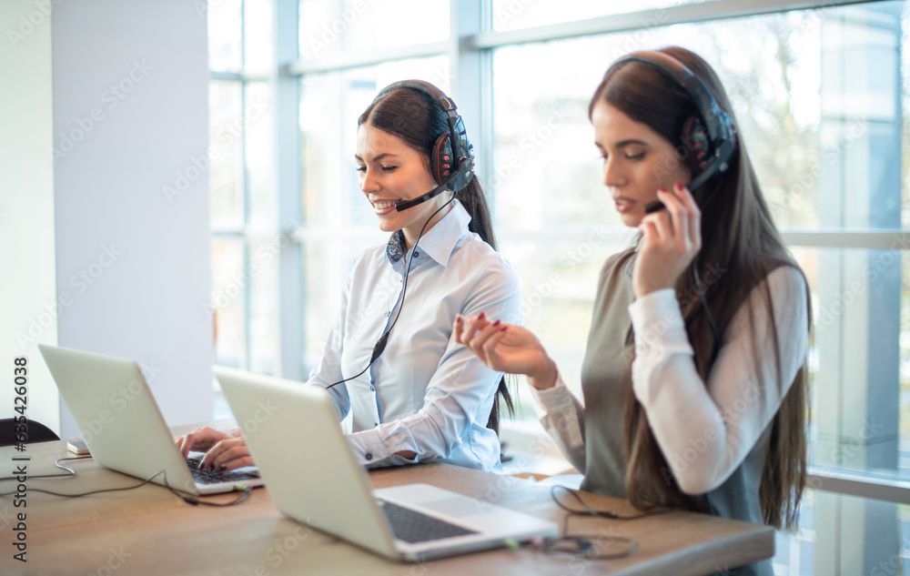 Two female support service operators with headset and laptops assisting customers during phone calls in bright office. Two female support service operators with headset and laptops assisting customers during phone calls in bright office.