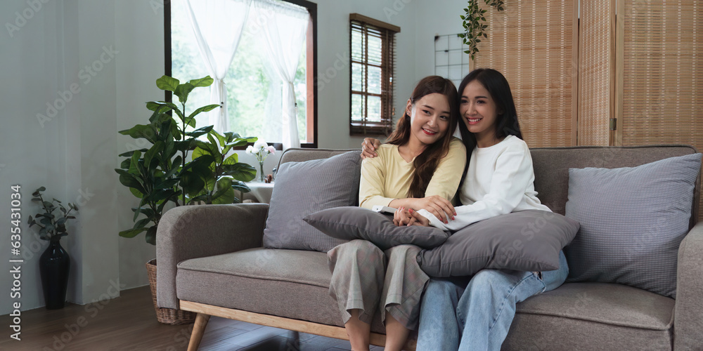 Asian young woman homosexual lesbian couple put on sweater sitting on sofa to watching cinema in living room at home Asian young woman homosexual lesbian couple put on sweater sitting on sofa to watching cinema in living room at home